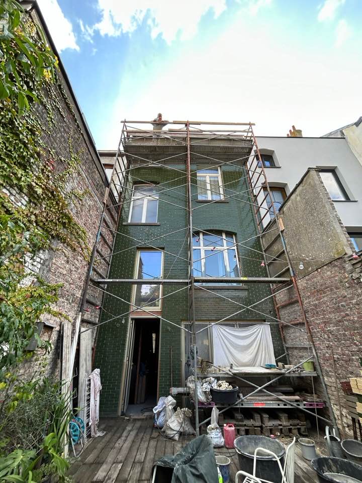 achtergevel met goudkleurig raam en steiger tijdens renovatie