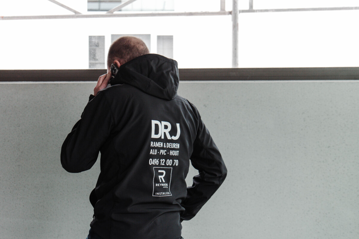 Professionele werkkledij met DRJ-logo en contactgegevens tijdens een werfbezoek voor een verandaproject.