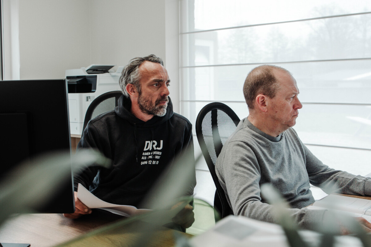 Twee medewerkers van DRJ RAMEN & DEUREN overleggen over een project met zonnewering in aluminium ramen – professioneel advies inbegrepen.